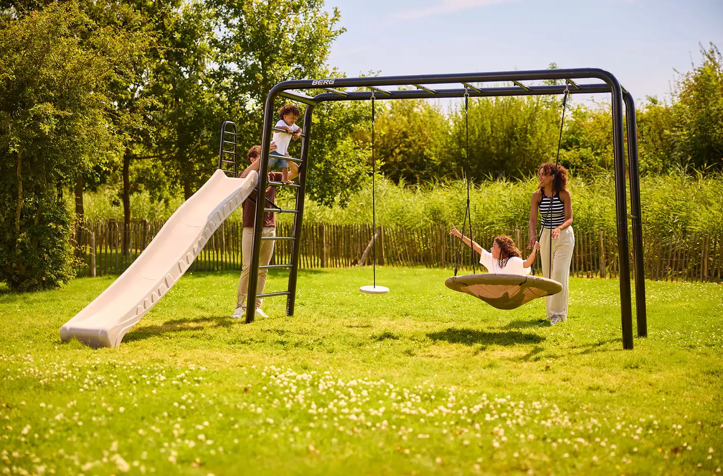 BERG PlayBase climbing frame in a garden with a slide, a nest swing and children playing